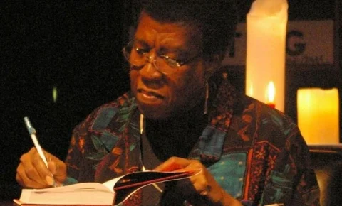 Mature black woman with wire-rimed glasses signing a book