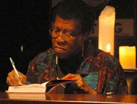 Mature black woman with wire-rimed glasses signing a book